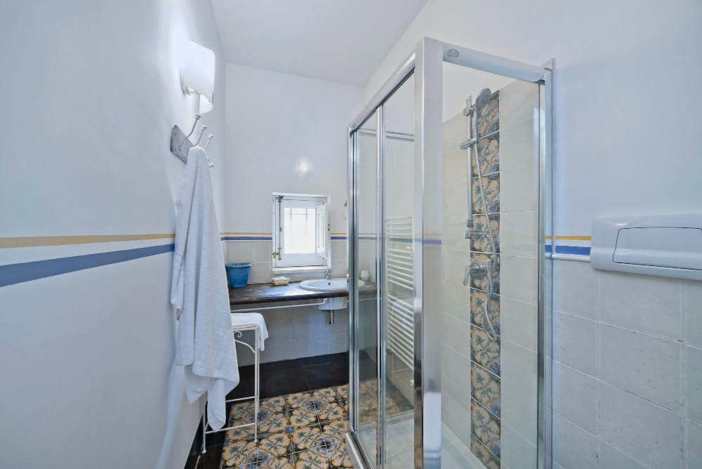 Salle de bain lumineuse avec carrelage à motifs et douche PMR sécurisée par une paroi vitrée