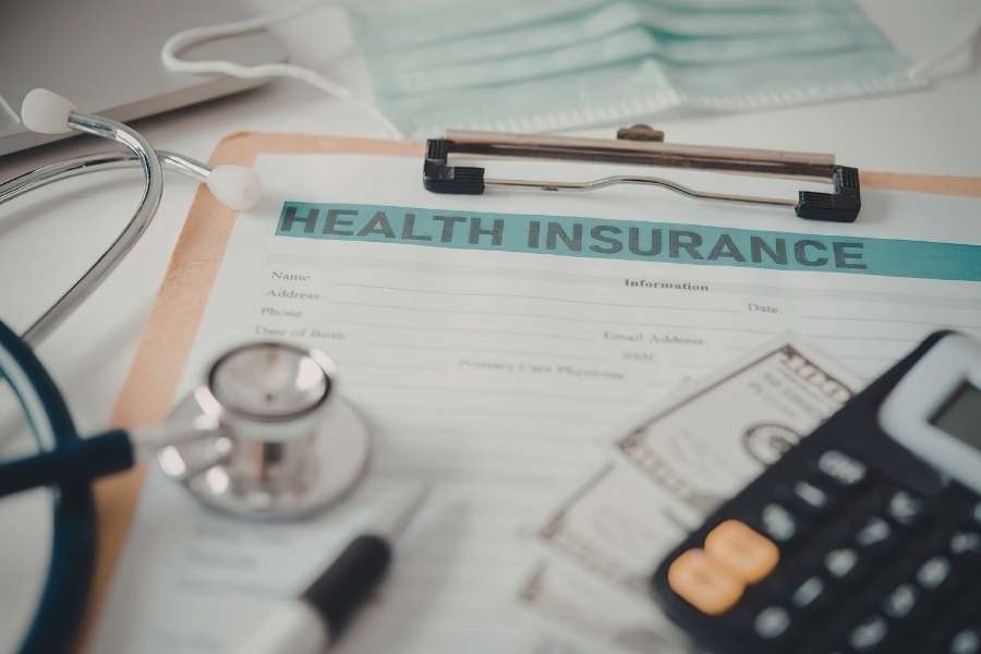 Un formulaire de mutuelle santé posé sur un bureau avec un stéthoscope, une calculatrice et des billets, symbolisant les démarches d'assurance médicale.