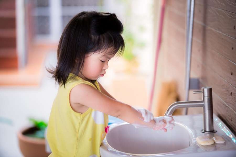 Une petite fille en haut jaune se lave soigneusement les mains avec de la mousse, une étape clé pour réussir la propreté.